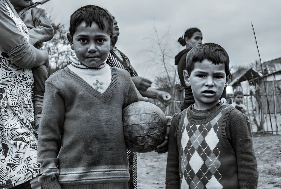 Two boys with a ball stand in a rural village setting. Black and white portrait.